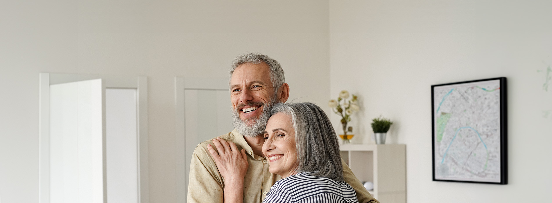 The image shows two adults embracing each other, with a third person standing behind them, all appearing to be in an indoor setting.