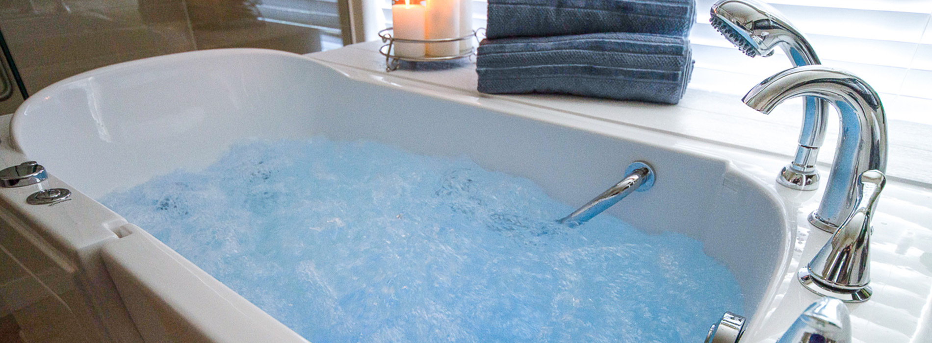 A bathtub filled with blue water, featuring a faucet and two handles, set against a dark background.