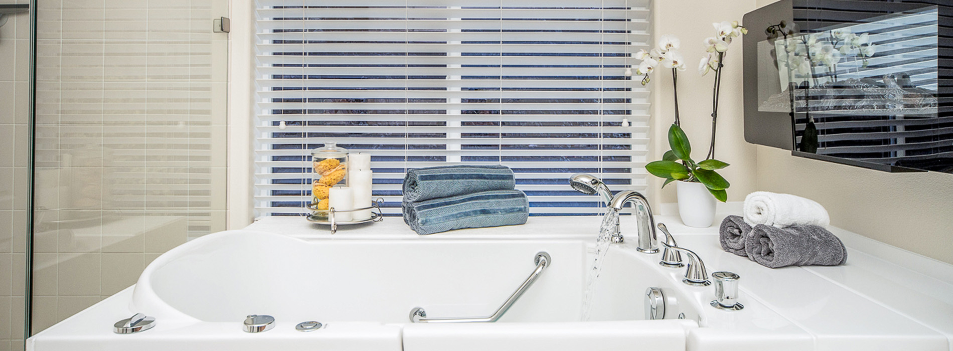 The image depicts a modern bathroom interior with a pristine white sink, a large mirror above it reflecting the room, blue blinds partially drawn, and various bathroom items on the countertop.