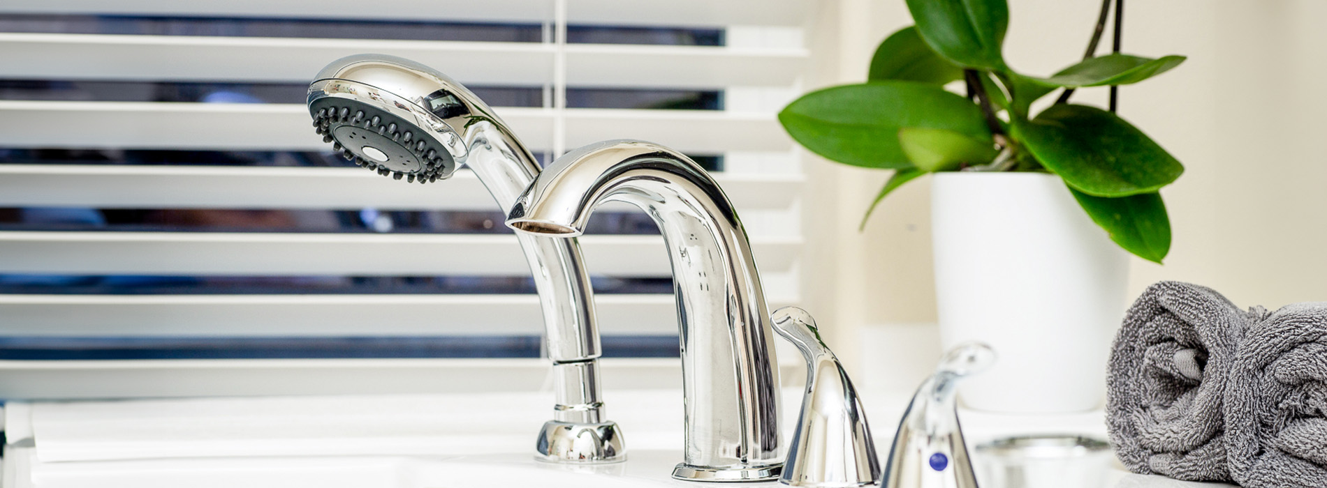 The image features a clear glass vase with a silver faucet on a white surface, set against a window blinds background.