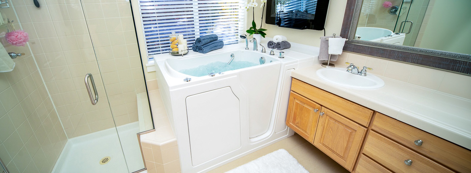 The image shows a bathroom with a sink, mirror, bathtub, and wooden cabinets.