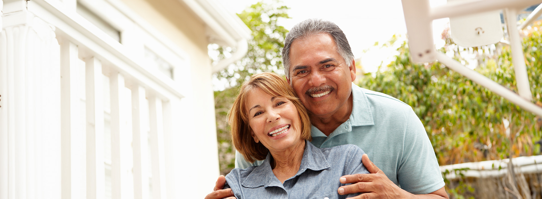 A man and woman are hugging each other in front of a house with a porch.