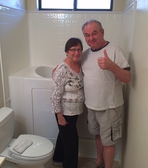 A man and woman in a bathroom, posing together with thumbs up, standing next to a toilet.