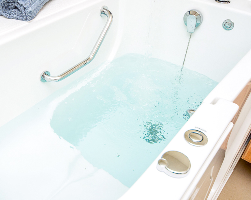 The image shows a white bathtub filled with blue water, located inside a bathroom.