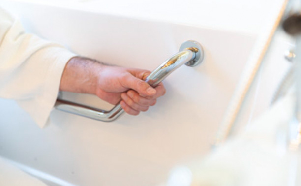 A hand holding a silver faucet handle over a white sink.