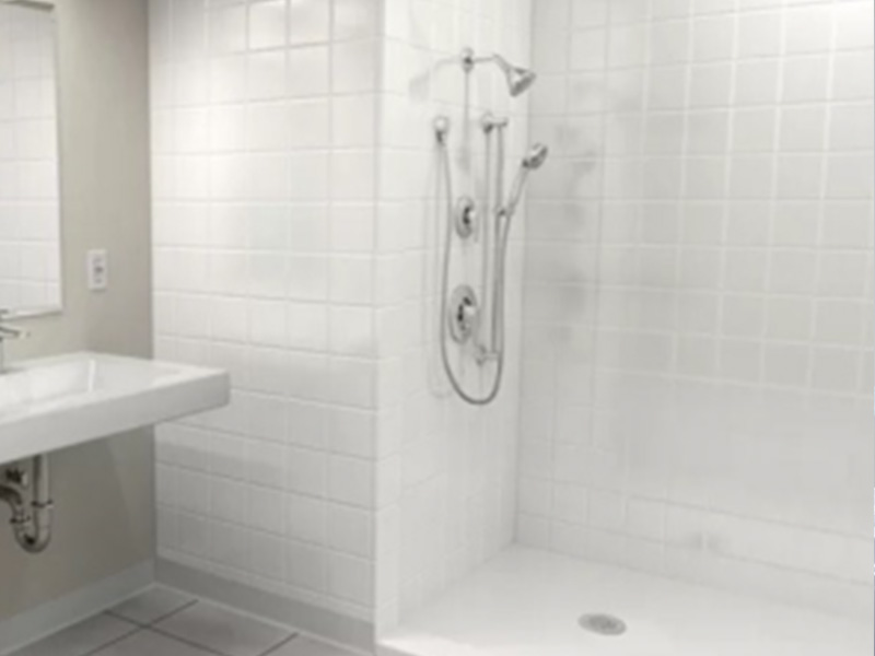The image shows a modern bathroom with white tiles on the walls, a large shower stall, a toilet, and a sink with a silver faucet.