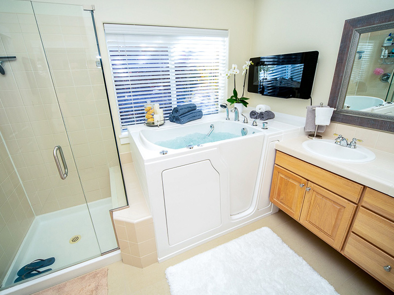 The image shows a modern bathroom interior with a large bathtub, a double sink vanity, a walk-in shower, a mirror above the sinks, and a well-lit space with neutral colors.