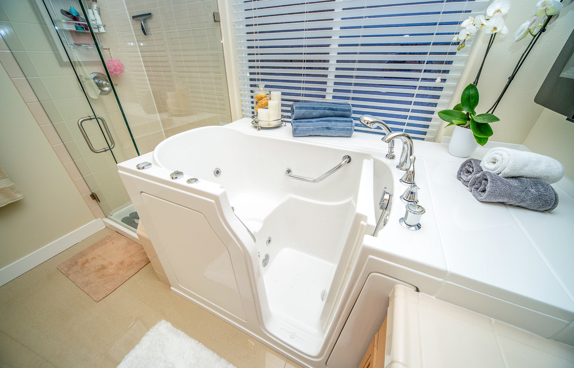 A well-maintained bathroom with a white bathtub, sink, and toilet, featuring blue window blinds and a neatly arranged space.