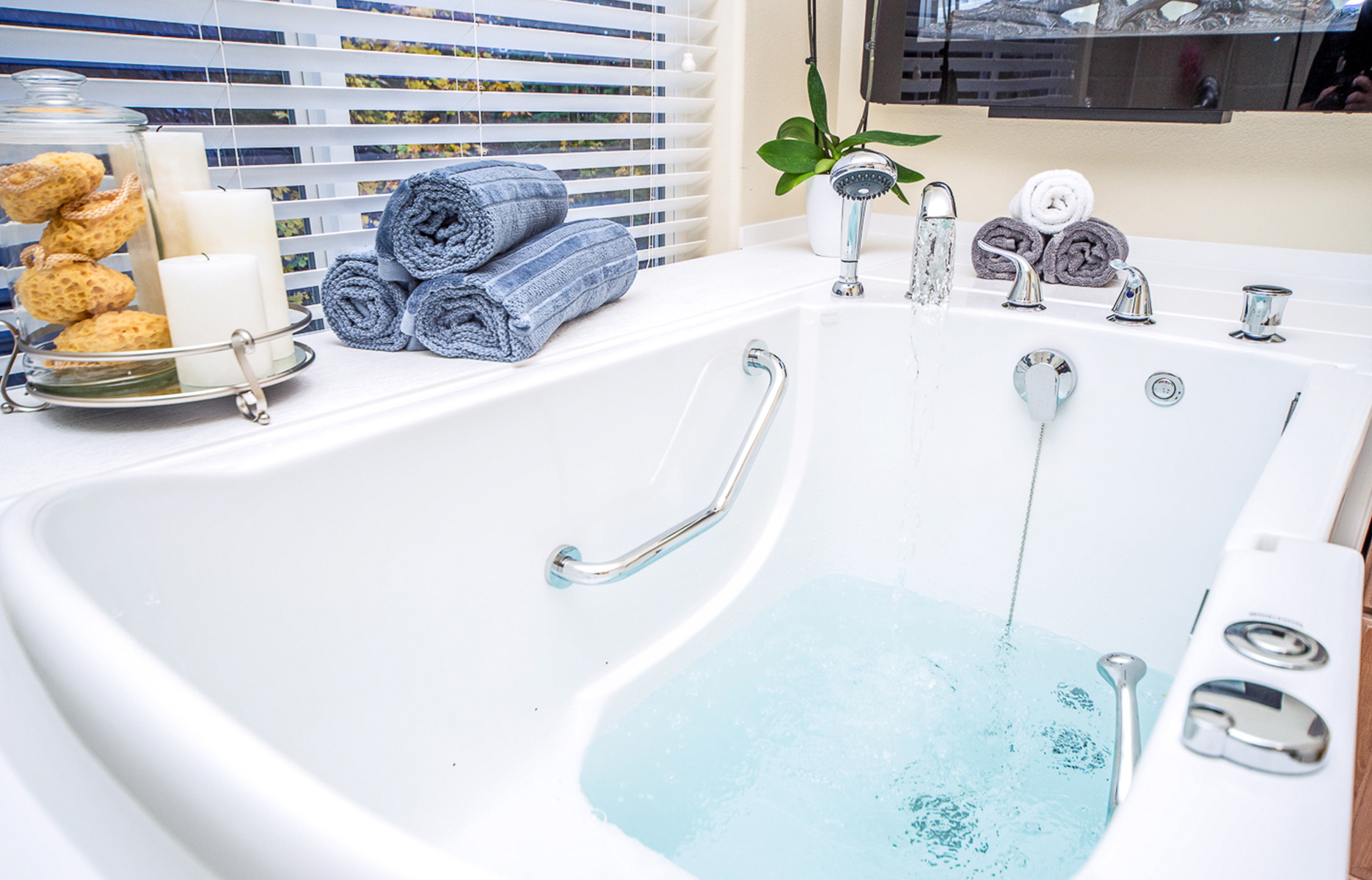 The image showcases a modern bathroom with a soaking bathtub, a walk-in shower, a large window with white blinds, and a neatly arranged sink area with towels and toiletries.